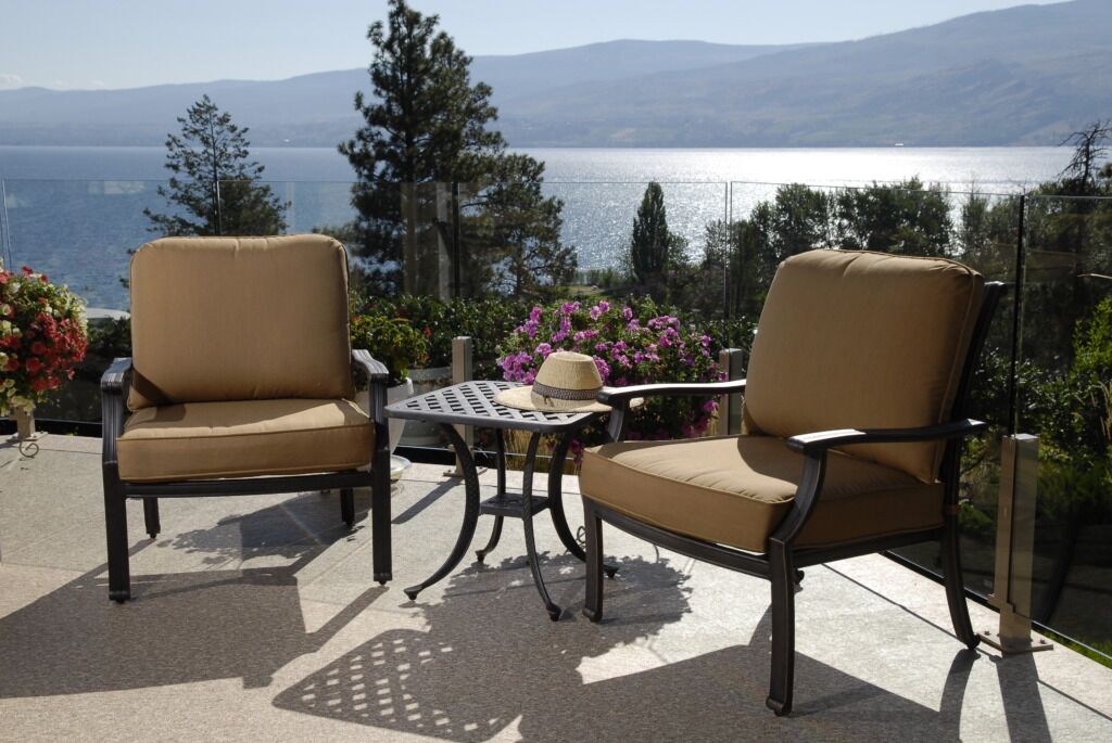 Two deck chairs with cushions and a deck table on a vinyl deck surface with a view of a lake in the background.